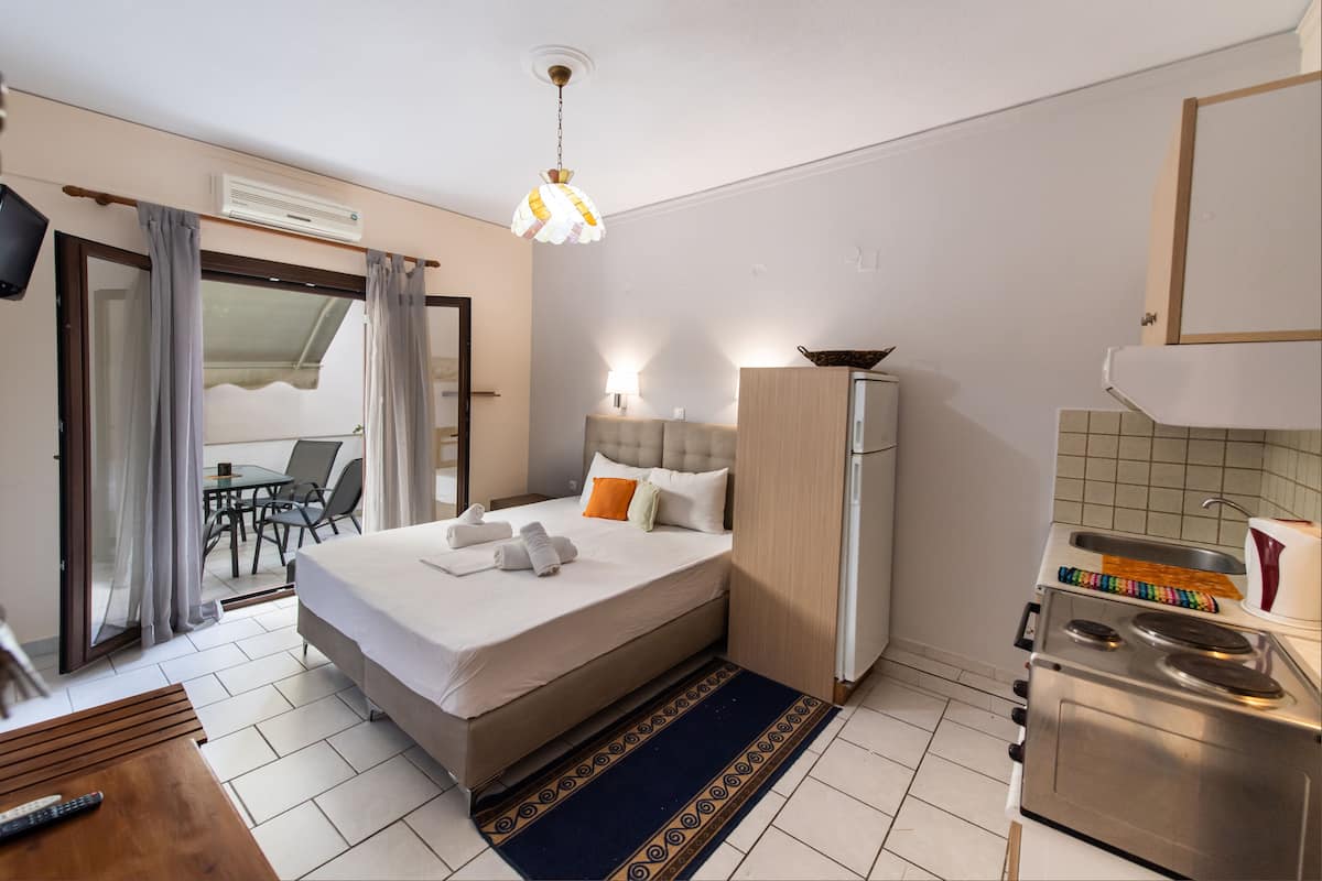 Quarto de hotel com cama, escrivaninha, cozinha compacta e área de refeições.