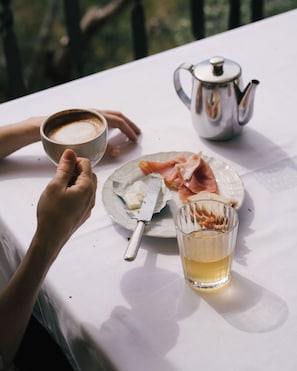 A table with a white tablecloth, a teapot, a cup of coffee, a plate with food, and a glass of tea. - Pensione Bencistà (Fiesole)