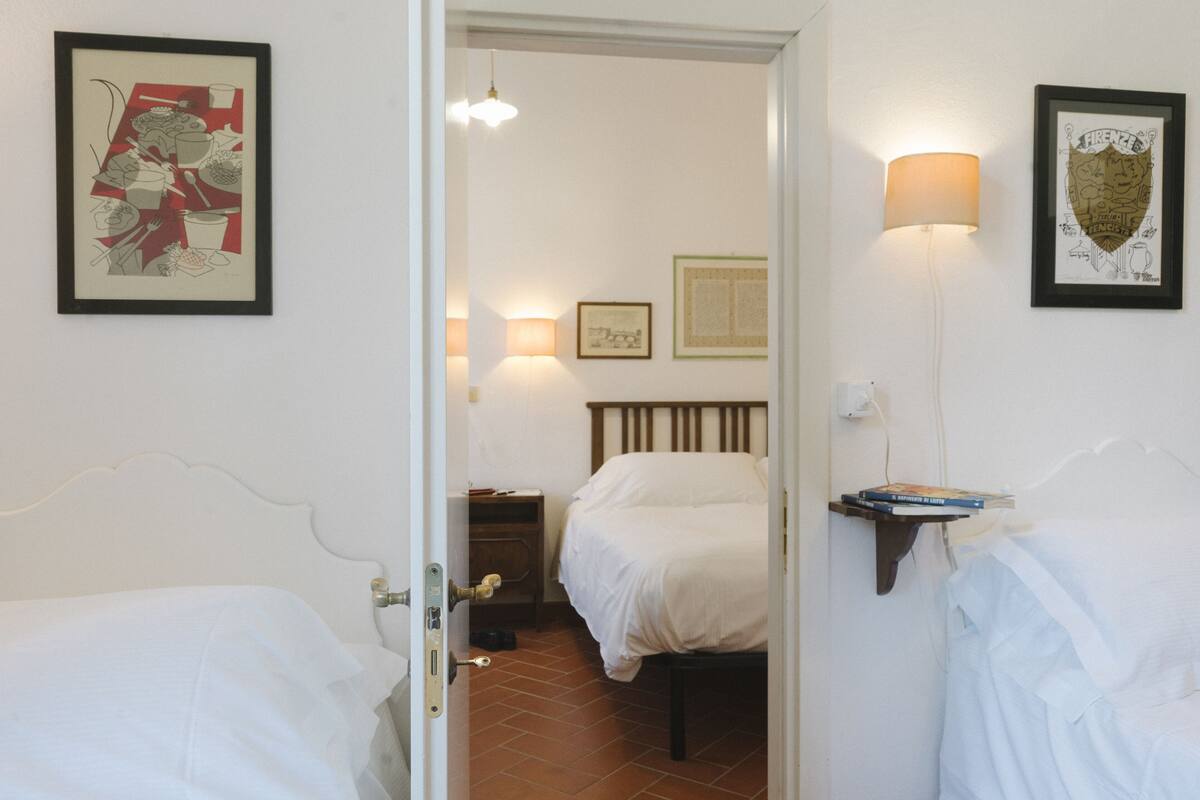 A hotel room with two beds, a nightstand, a lamp, and artwork on the walls.