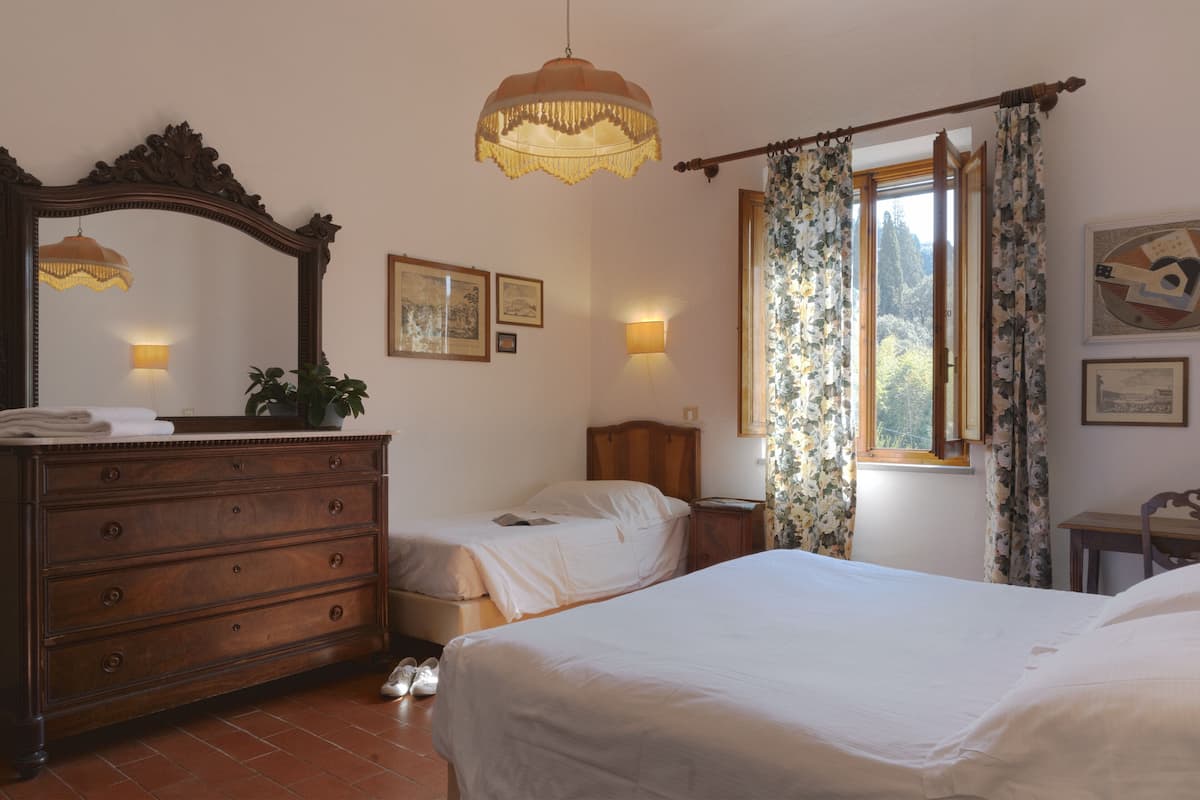 A bedroom with two beds, a dresser, a mirror, and a window with curtains.