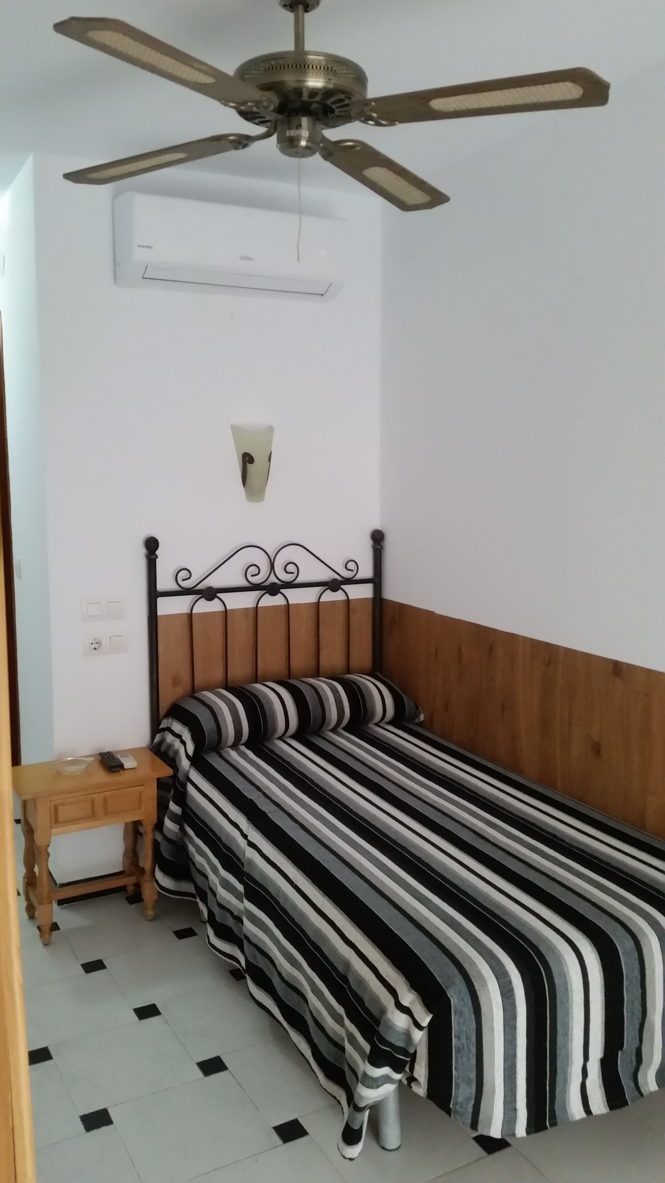 A bedroom with a bed, a nightstand, a ceiling fan, and a wall-mounted air conditioner.