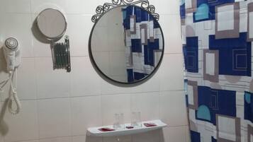 Un baño con lavamanos pedestal, un espejo redondo, inodoro, bidé y cortina de ducha con estampado geométrico.