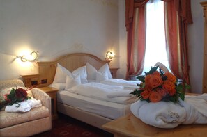 A hotel room with a bed, a chair, a nightstand, and a table with a bouquet of roses. - Excelsior (Cavalese)