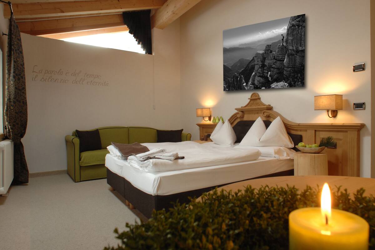 A hotel room with a bed, a green sofa, a wall with a framed picture, and a lit candle on a table.
