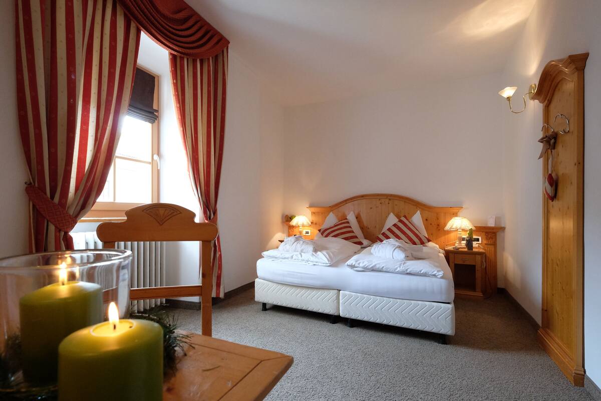 A cozy bedroom with a bed, two bedside lamps, a wooden headboard, a nightstand, and a window with curtains.