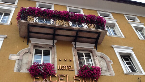 A hotel named "HOTEL EXCELSIOR" with a yellow facade, white window frames, and a balcony with pink flowers. - Excelsior (Cavalese)