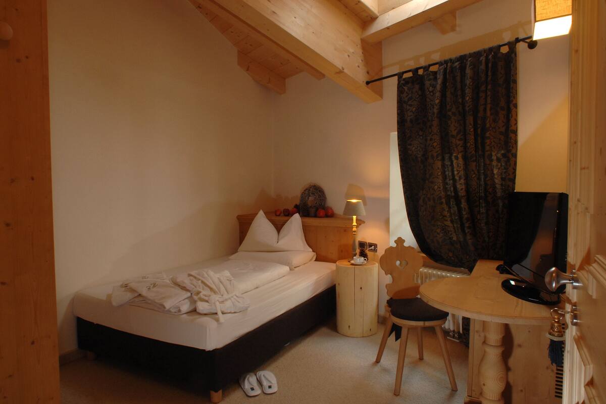 A bedroom with a bed, a chair, a small table, and a mirror.