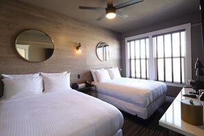Habitación de hotel con dos camas, un escritorio, un ventilador de techo y ventanas amplias.