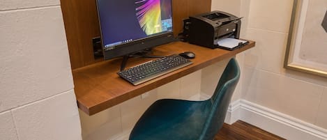 Escritorio en esquina con monitor Lenovo, teclado e impresora. Una silla color turquesa está colocada al frente.