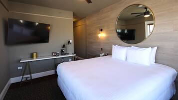 A hotel room with a large bed, a desk with a lamp, a flat-screen TV, and a ceiling fan.