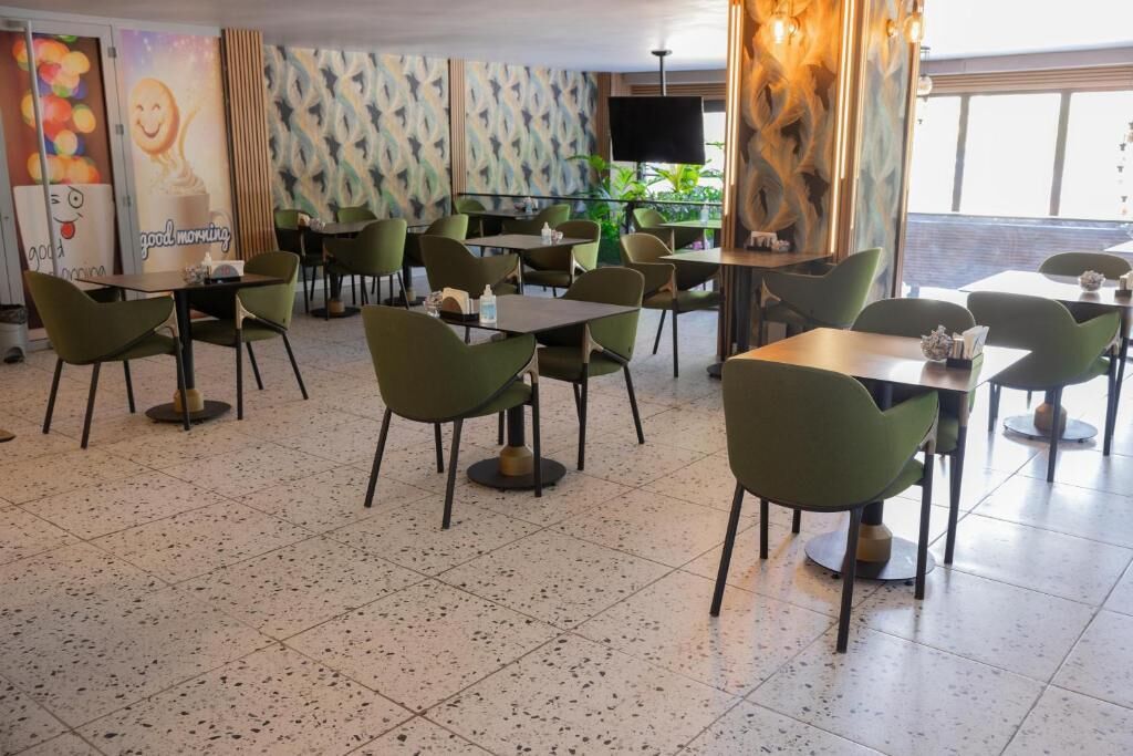 Un restaurante con sillas y mesas verdes, una pantalla de televisión grande y un mural en la pared.
