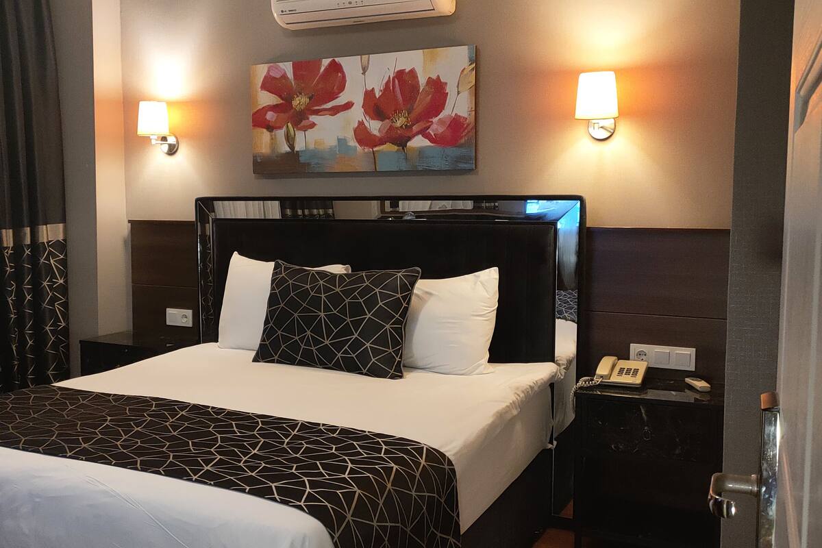 A hotel room with a large bed, two bedside lamps, a painting, and a nightstand with a phone.