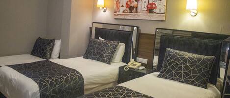 A hotel room with two beds, each with a geometric-patterned bedspread and matching pillows. There are bedside tables with lamps and a wall-mounted clock.