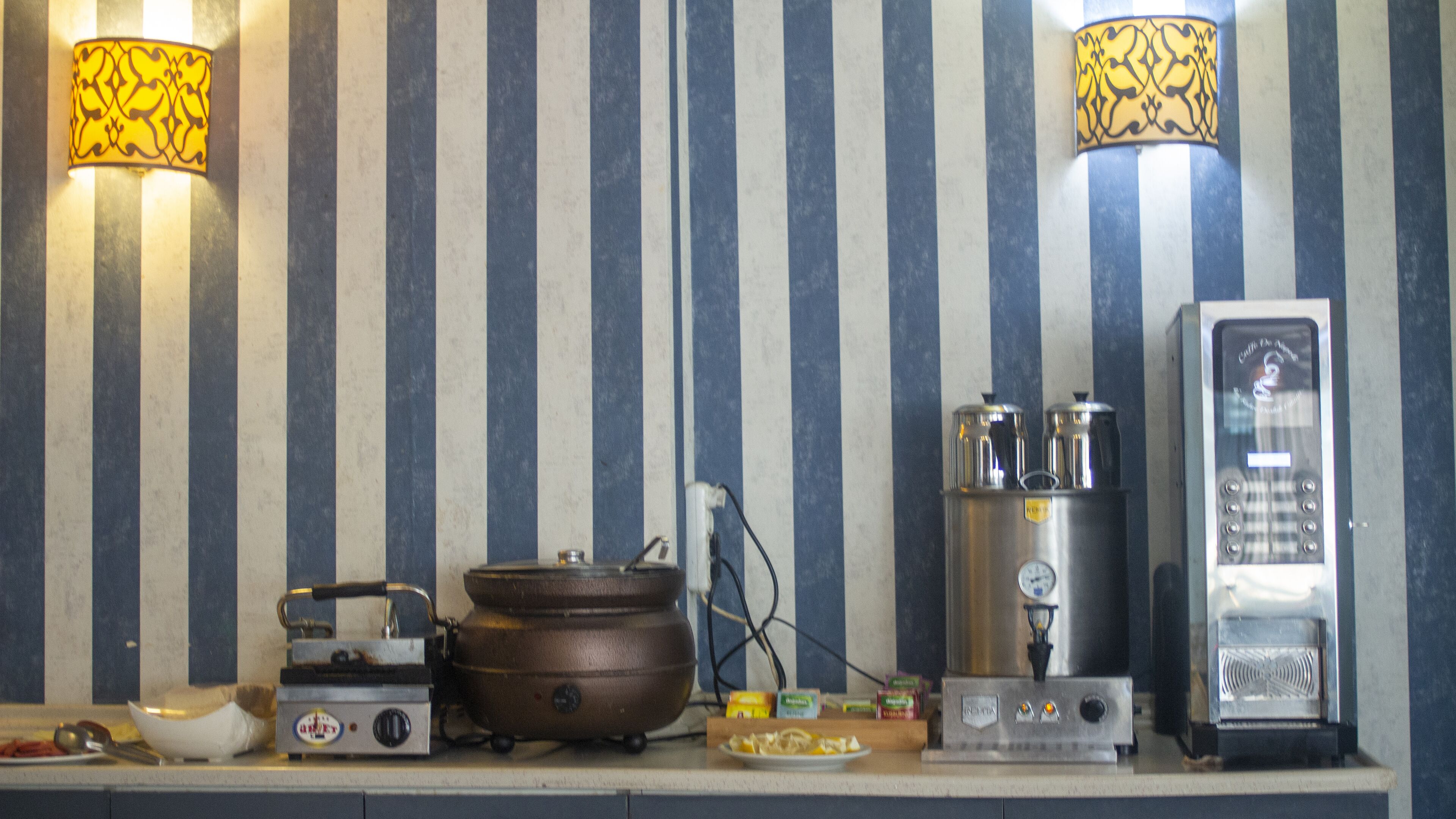 A kitchen with striped wallpaper, a stove, a kettle, and a coffee machine.