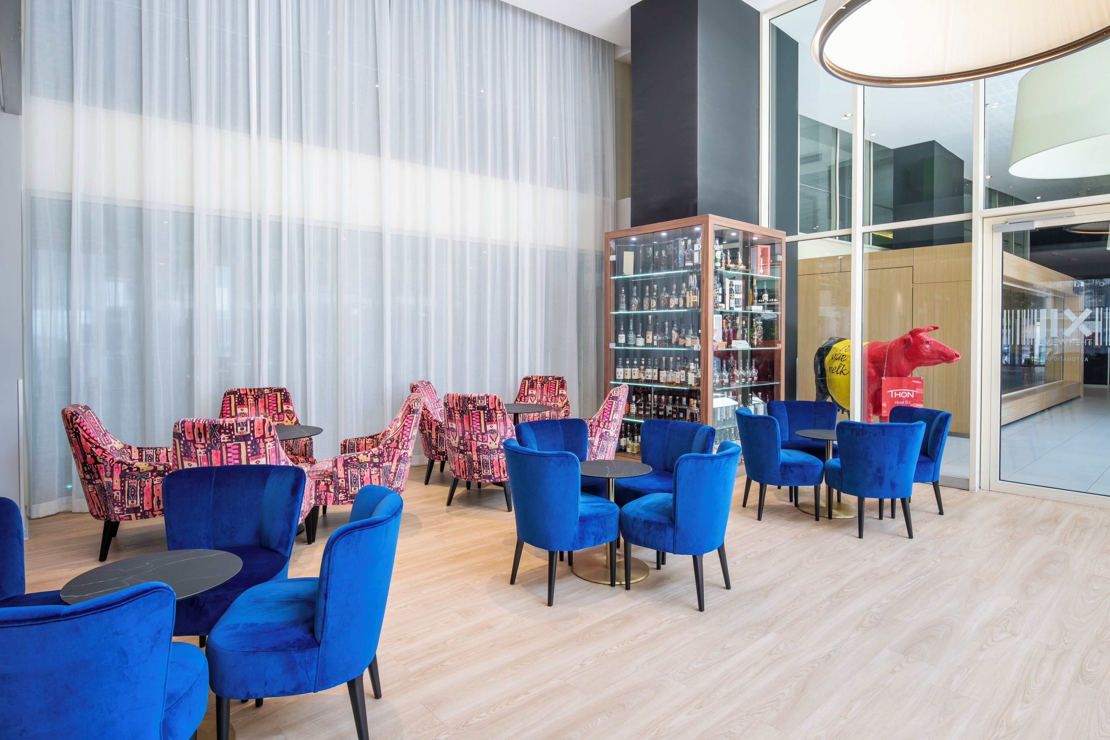 Een moderne zithoek met blauwe stoelen en een patroon van stoelopstellingen, een boekenkast en een rode sculptuur.