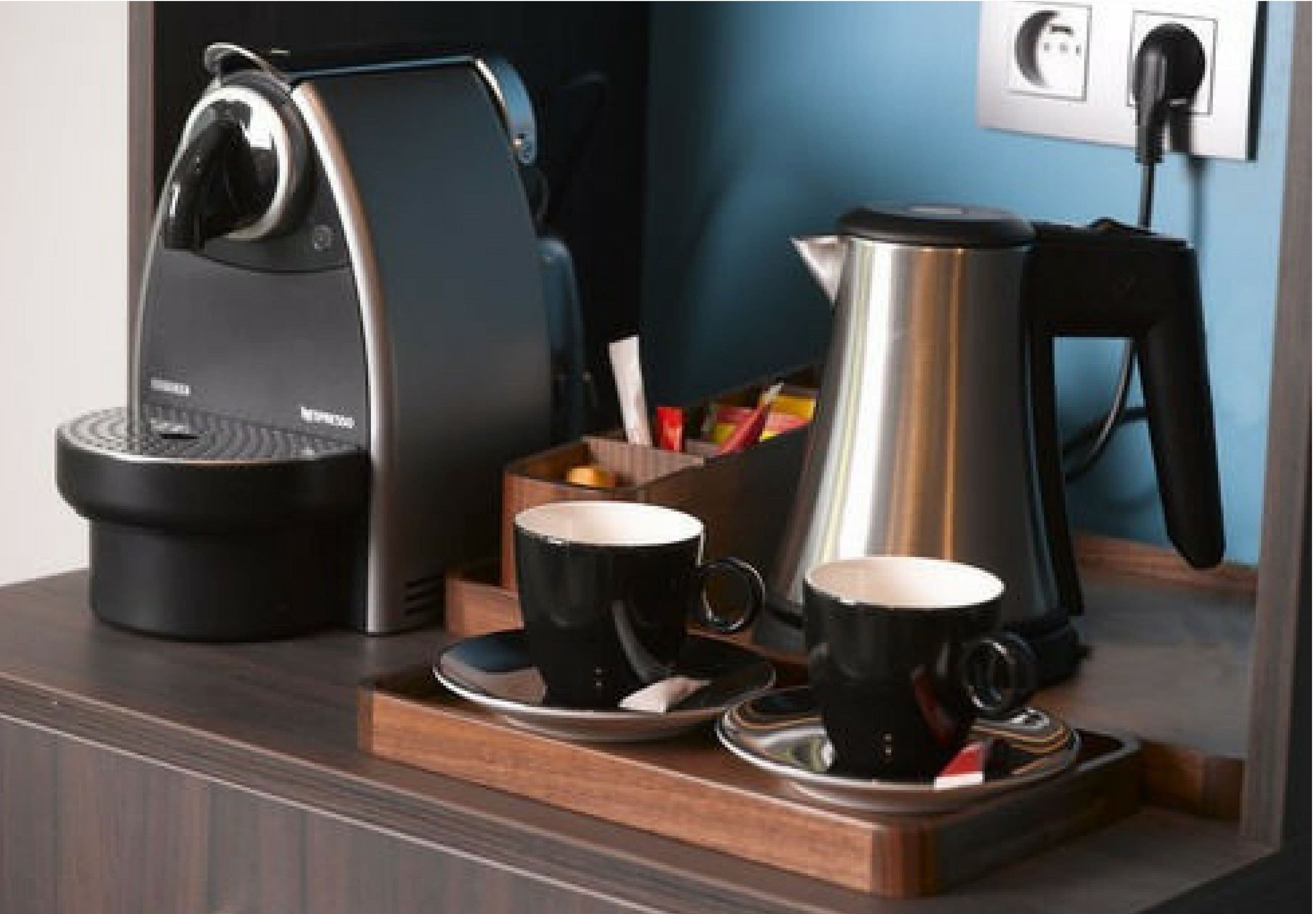 Una estación de café con una cafetera, dos tazas y una termo sobre una bandeja de madera.