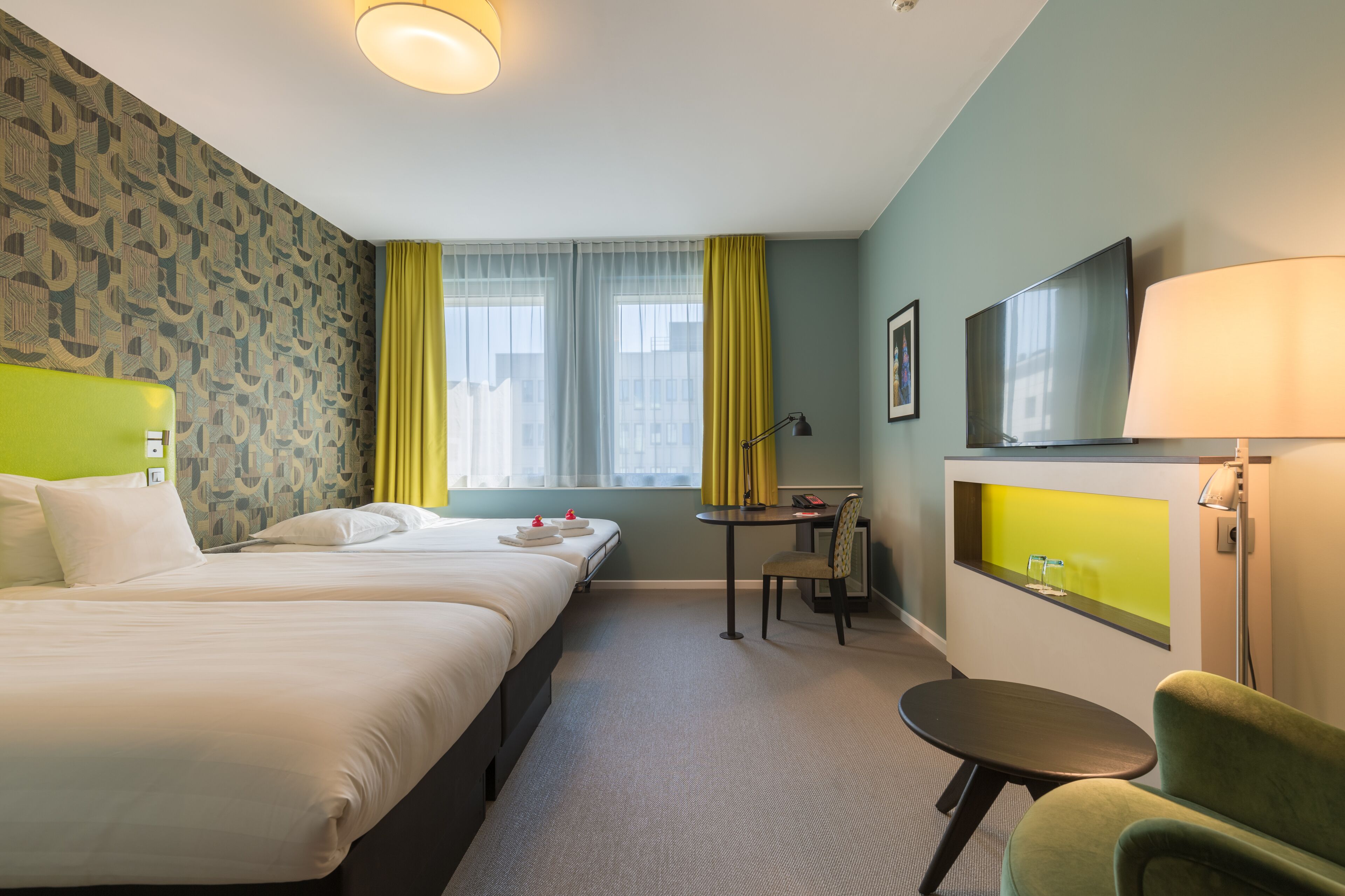Habitación de hotel con dos camas, un escritorio, una silla, un televisor y una ventana con cortinas.