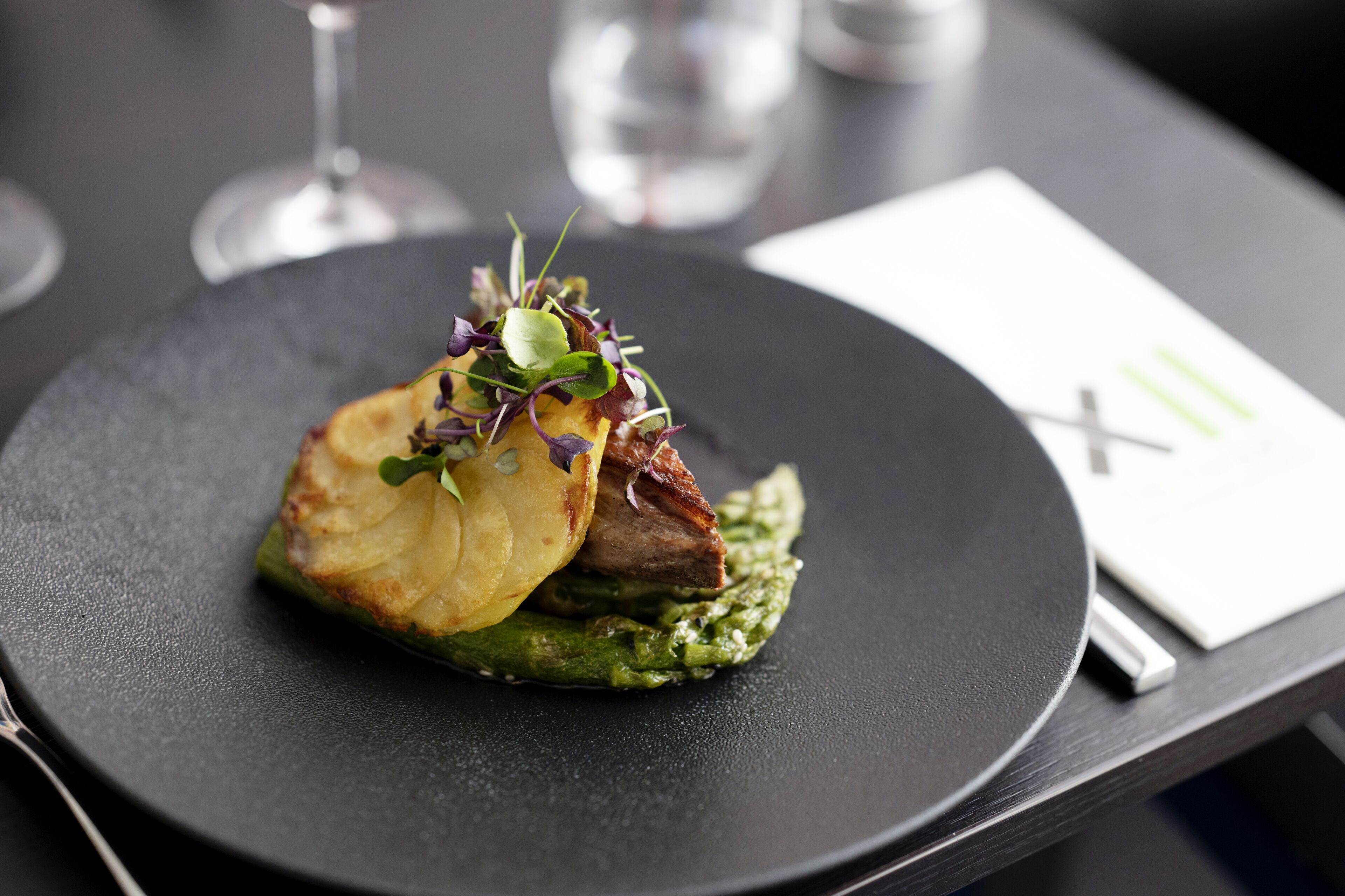 A plate of food with a green sauce base, topped with a piece of meat and a potato slice, garnished with greens.