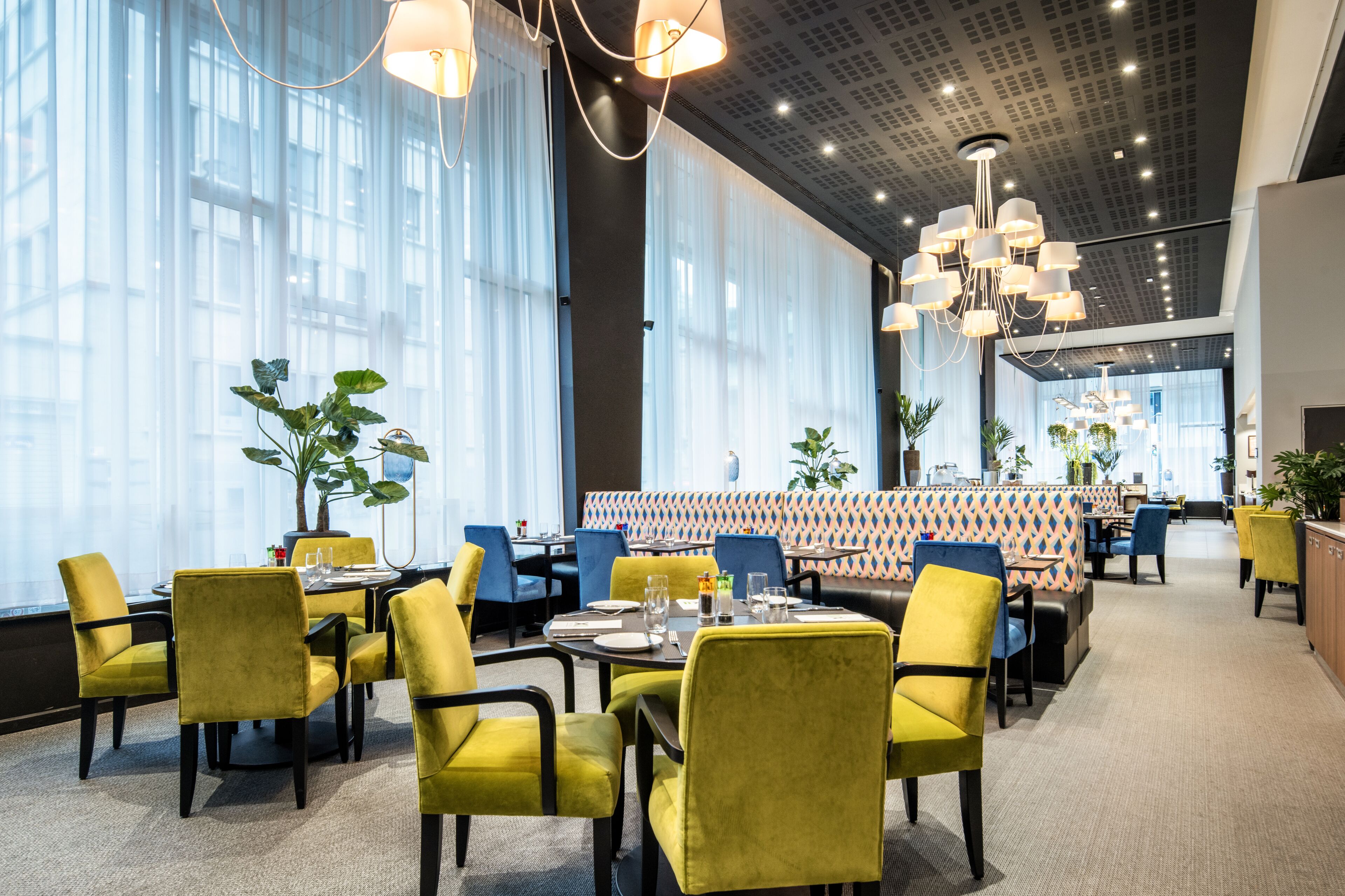 A modern restaurant with yellow chairs, a patterned booth area, and large windows.