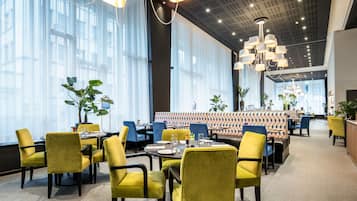 A modern restaurant with yellow chairs, a patterned booth area, and large windows.