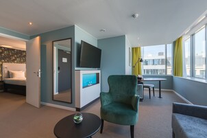 Habitación de hotel con cama, televisor, escritorio con silla y ventana con cortinas.