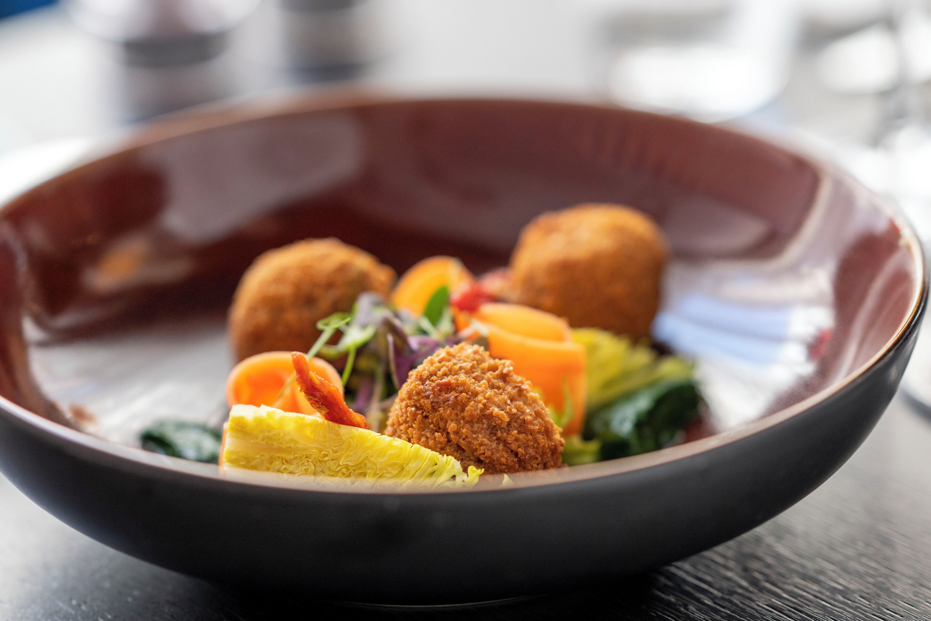 A bowl of food with breaded balls, vegetables, and a slice of lemon.