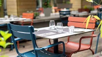 Comedor con mesas dispuestas para dos, sillas metálicas y una combinación de asientos rojos y azules.