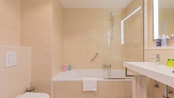 A modern bathroom with a bathtub, a shower, and a toilet. There are toiletries on the sink and a towel hanging on the wall.