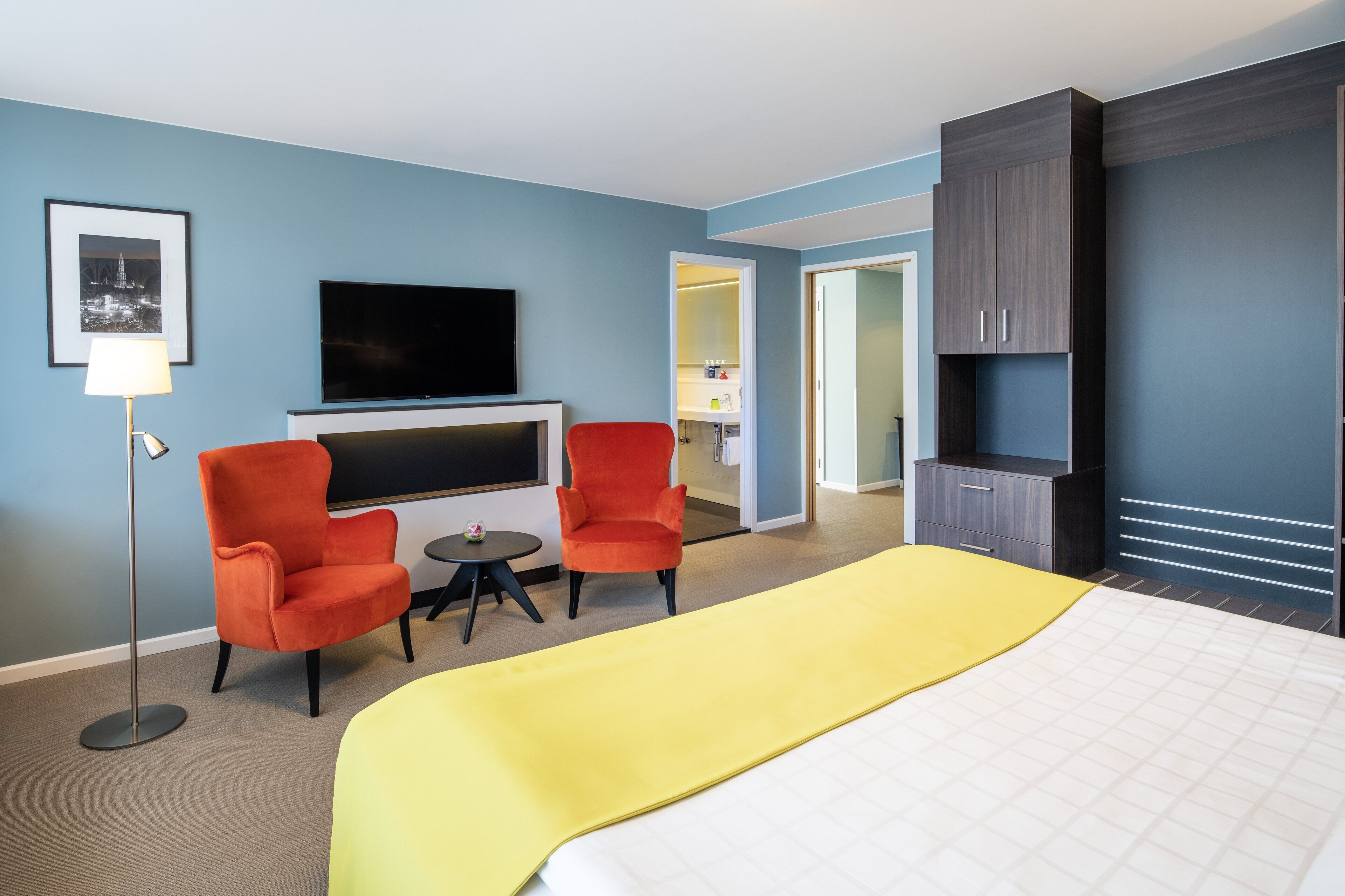 Una habitación de hotel con una cama, dos sillones, una mesita, un televisor y un armario.