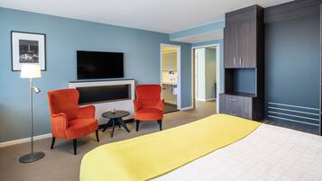 Una habitación de hotel con una cama, dos sillones, una mesita, un televisor y un armario.