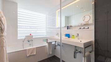 Un baño moderno con bañera, tocador con espejo y ventana con persianas.