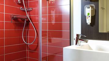 A modern bathroom with red tiled walls, a glass shower enclosure, a white sink, and a mirror.