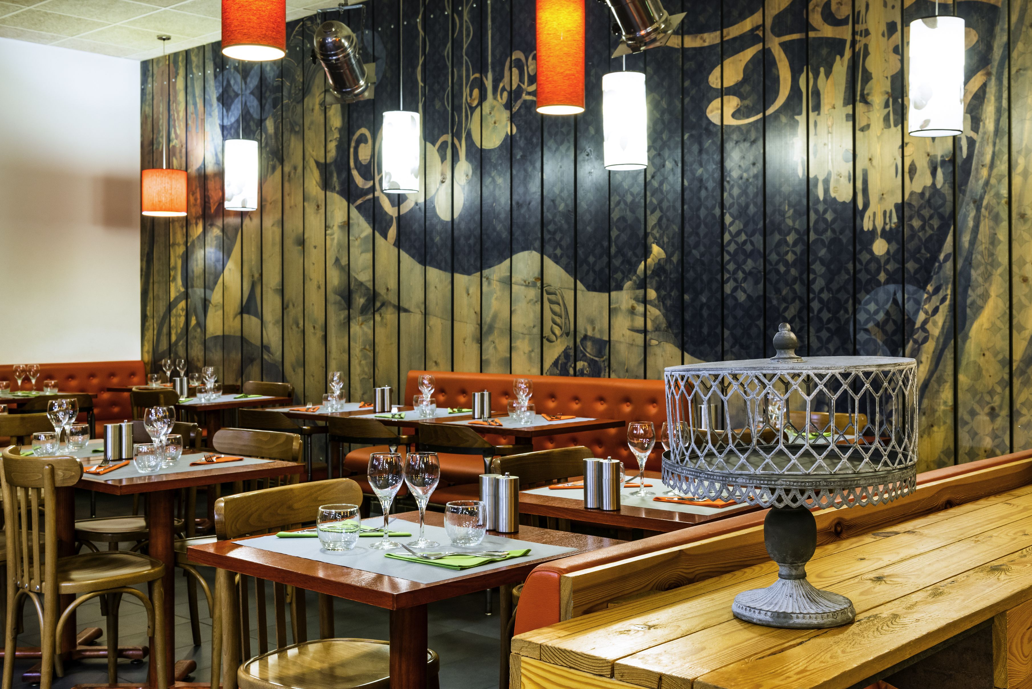A restaurant interior with wooden walls, tables with chairs, and hanging pendant lights.