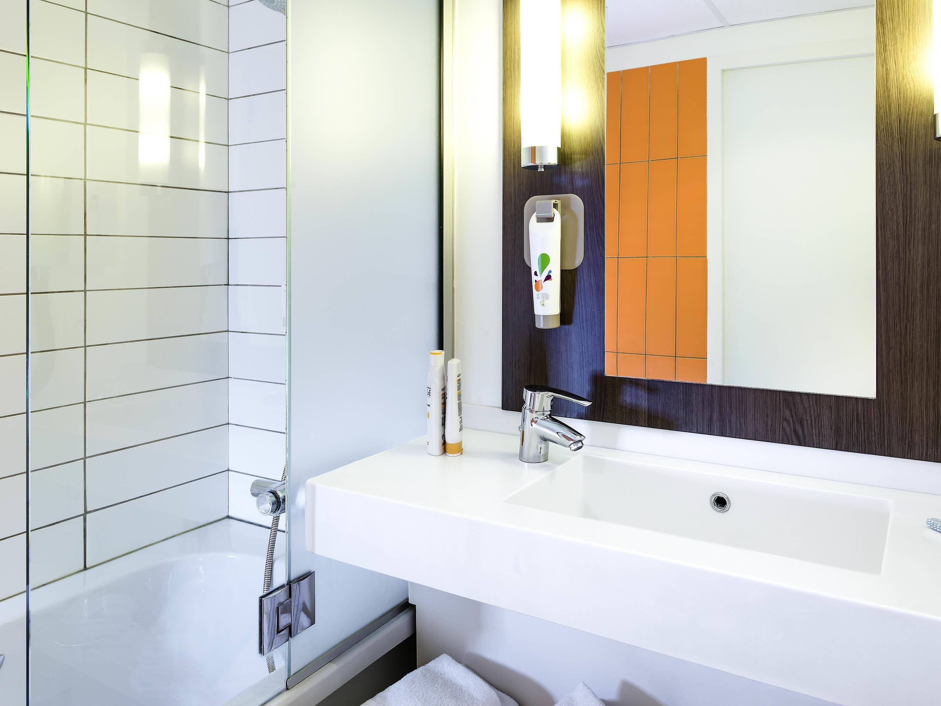 A modern bathroom with a white sink, a large mirror, and a towel rack.