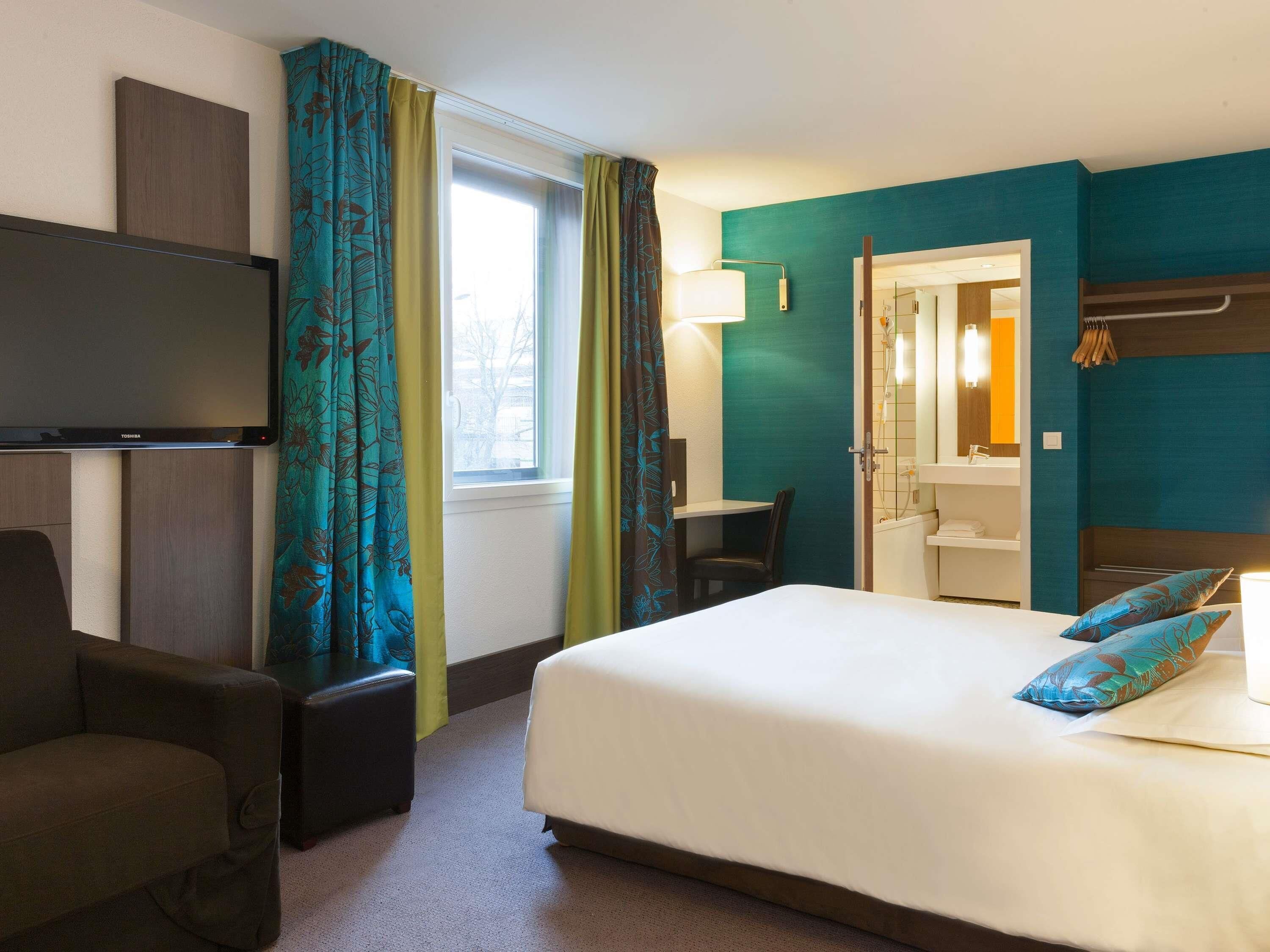 A hotel room with a bed, a desk, a chair, a television, and a bathroom.