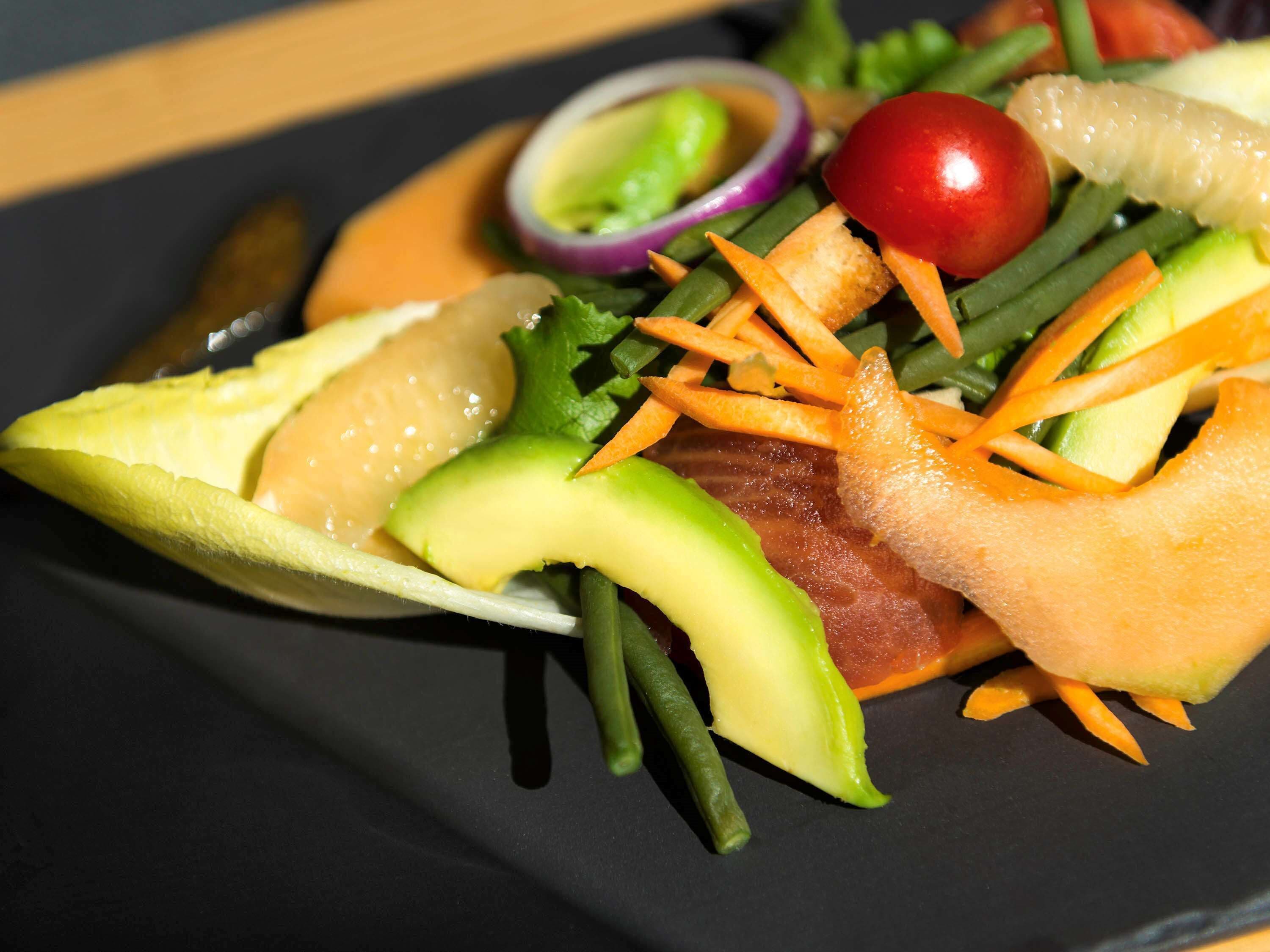 A close-up of a salad with various vegetables and a slice of avocado.