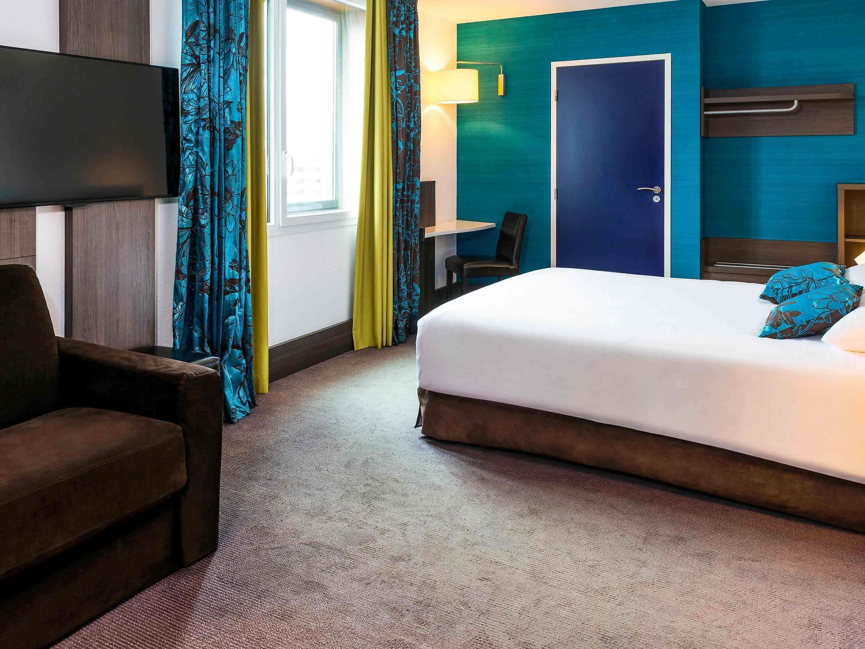 Une chambre d’hôtel avec un lit, une chaise, un bureau, une télévision et une porte.