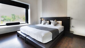 Um quarto moderno com uma cama grande, um banco no rodapé da cama e uma janela com vista para o verde.