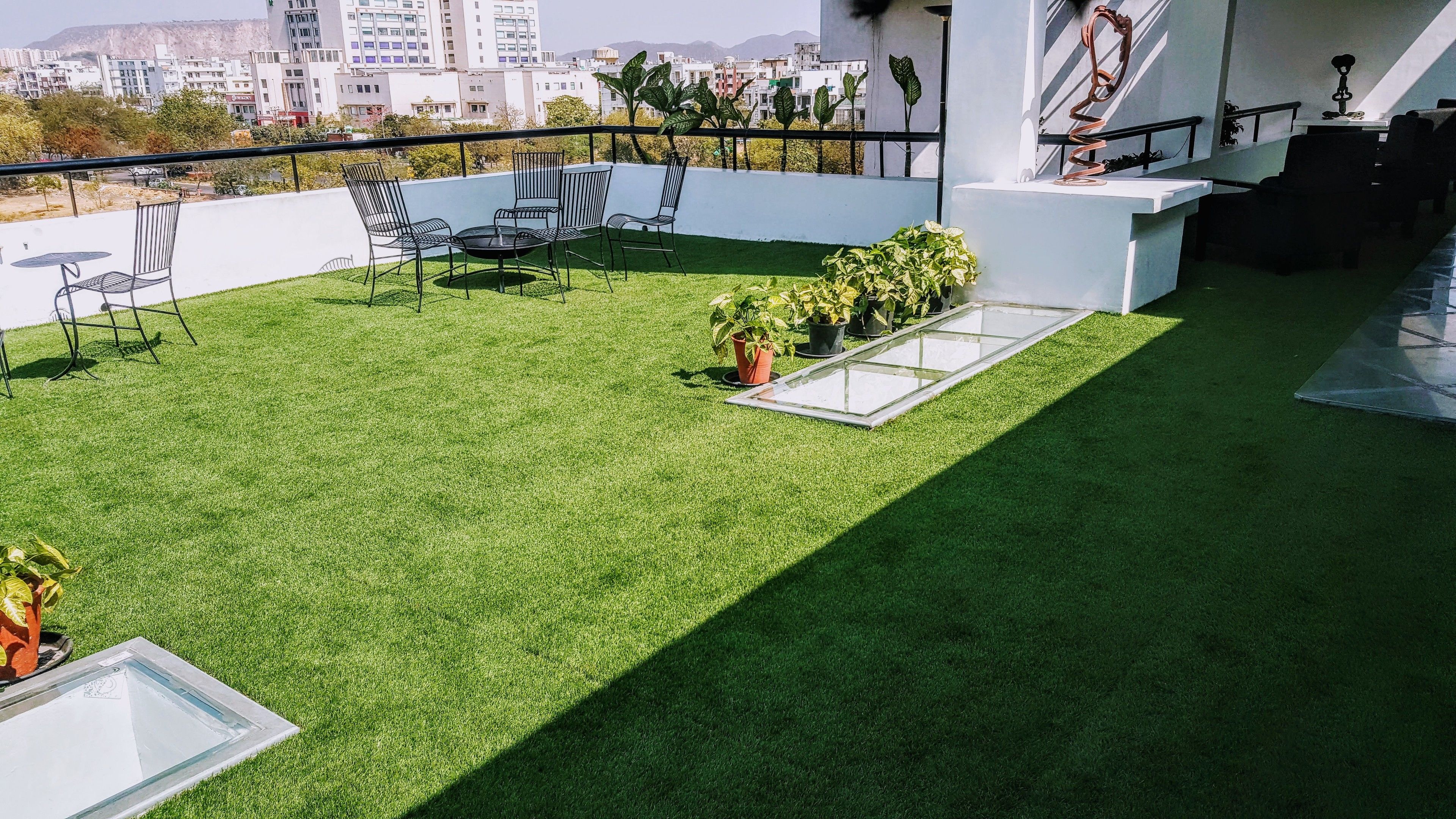 Una terraza en la azotea con césped artificial, sillas de metal, una mesita y plantas en macetas.