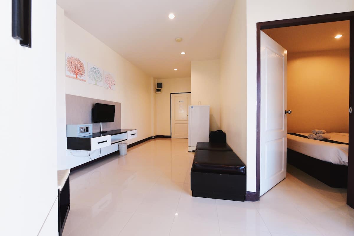 Habitació d'hotel moderna amb televisió de pantalla plana, una banca, un llit i una porta que condueix a una altra habitació.