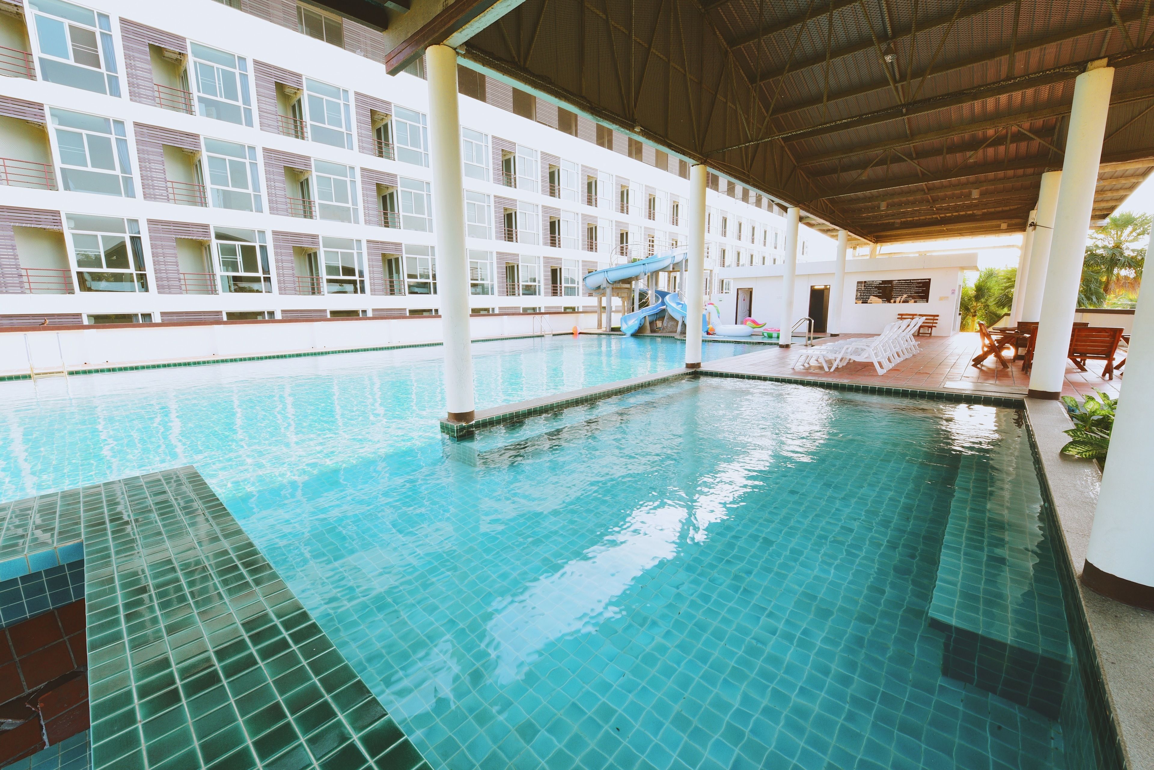 A swimming pool with a water slide, lounge chairs, and a covered area with a view of a building.