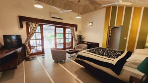 A hotel room with a bed, a desk with a TV, a chair, and a view of the outdoors through large windows. - Casa Vagator (Vagator)