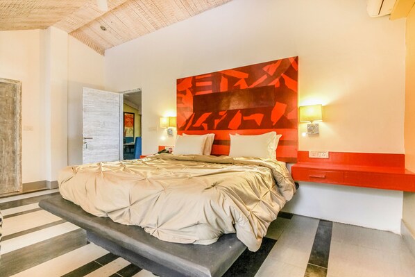 A modern hotel room with a bed, a headboard with abstract art, bedside lamps, and a red accent wall.