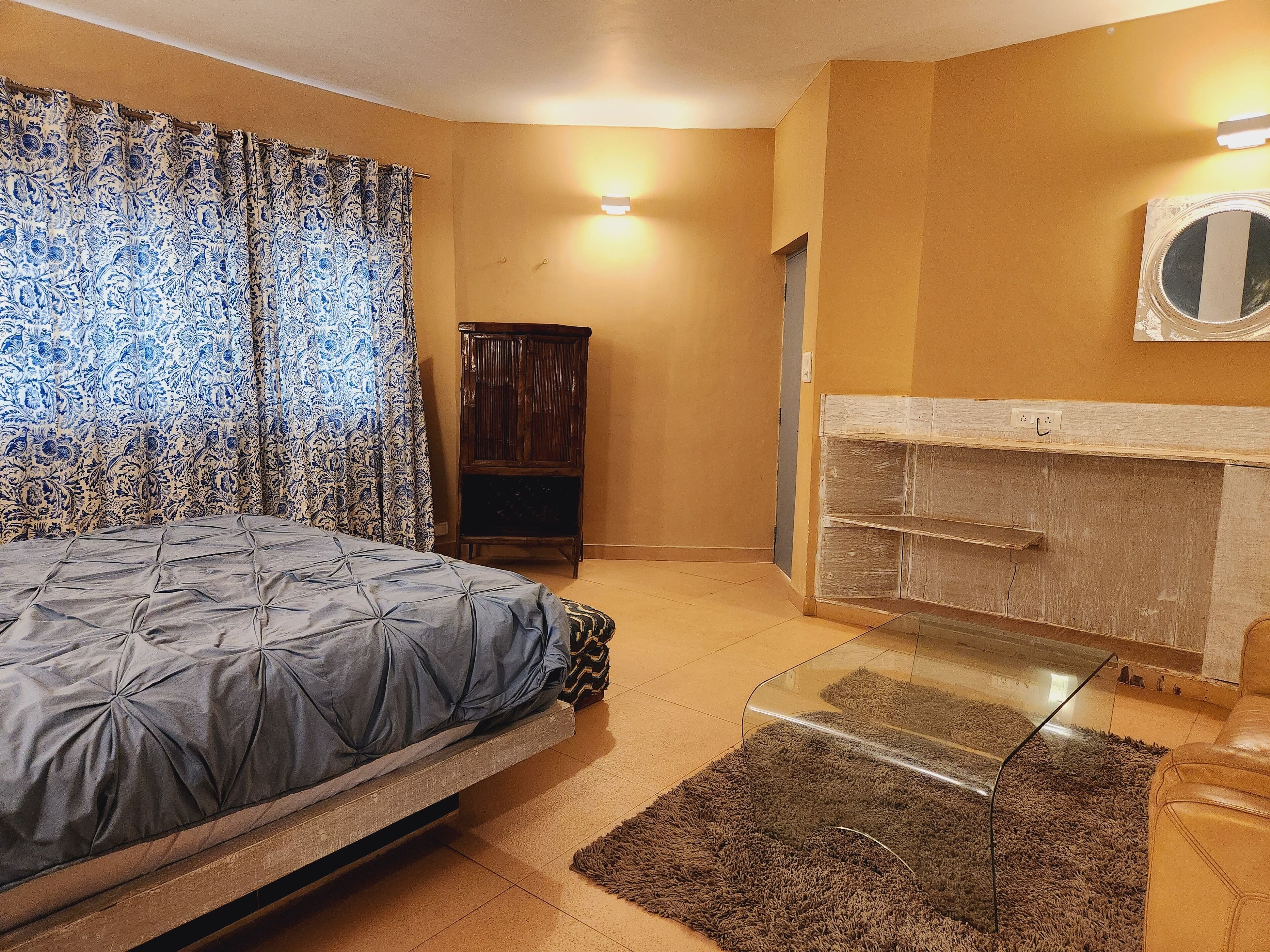 A bedroom with a bed, a wooden cabinet, a mirror, and a fireplace.