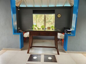 A room with a wooden desk, two chairs, a window with a view of trees, and a clock on the wall. - Casa Vagator (Vagator)