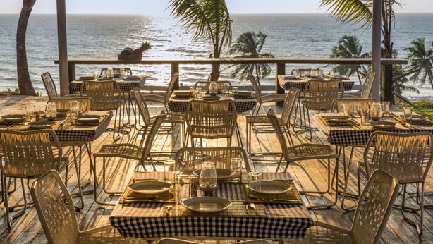 An outdoor dining area with tables and chairs arranged for guests, overlooking the ocean. - Casa Vagator (Vagator)