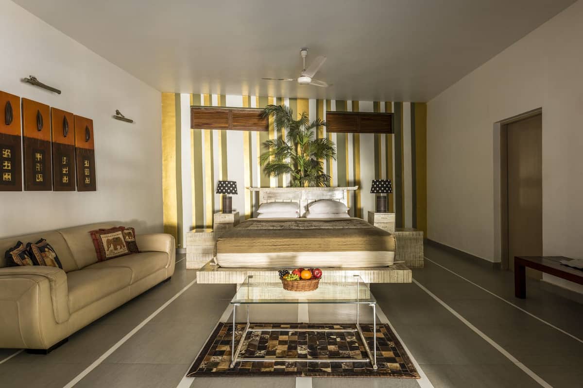 A modern bedroom with a large bed, a glass coffee table, a sofa, and a striped wall.
