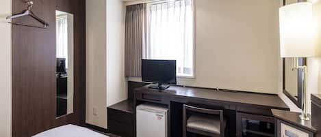 A hotel room with a bed, a desk with a computer, a TV, a mini-fridge, a chair, and a mirror.