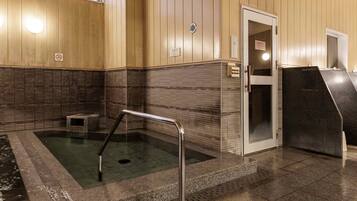 Sala de sauna con un banco de piedra, un escalón que lleva al agua y una puerta con un cartel.