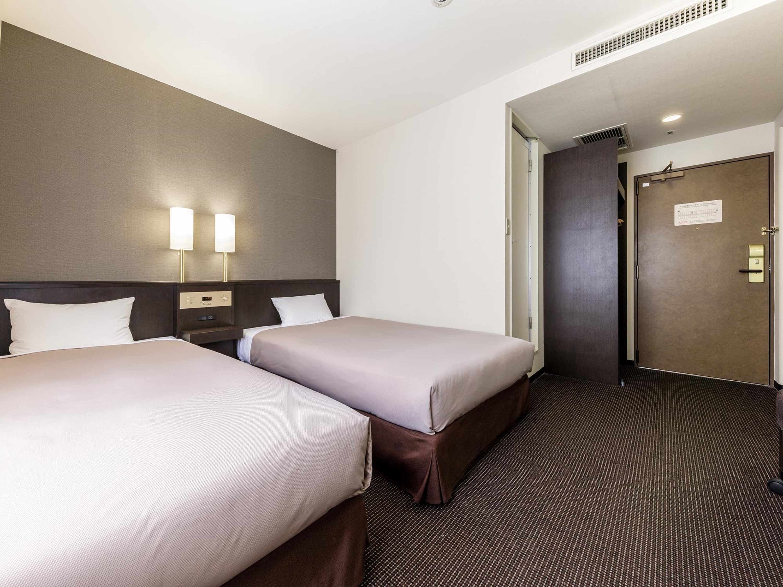 A hotel room with two beds, a nightstand, a lamp, and a door with a sign.
